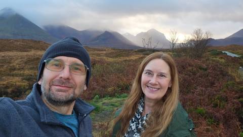       Two people smiling with scenic mountains in the background.
  