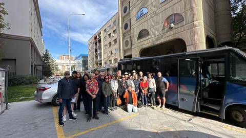 A large group of tourists in front of a tour bus in an urban setting.