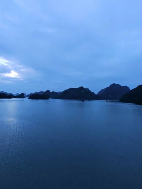       Halong Bay at dusk with darkened silhouettes of islands.
  