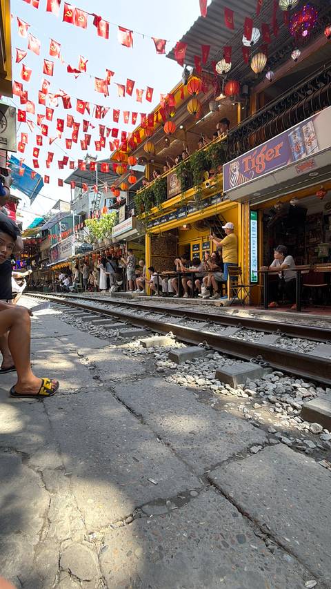       People sitting at cafes along train tracks in an urban area.
  