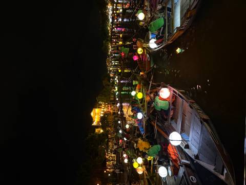       Boats on a river lit by colorful lanterns at night.
  