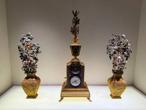 A decorative clock with two ornate vases beside it, displayed under soft lighting.