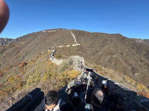 A section of the Great Wall of China stretching across a mountain landscape under a clear blue sky. Tourists walk along the wall.