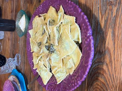       Plate of ravioli garnished with pepper and cheese on a rustic table.
  
