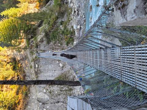 Suspension bridge crossing a roaring river with people walking.