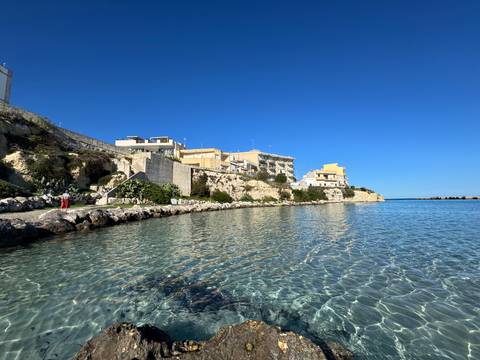 Coastal view of buildings along a rocky shoreline with clear blue water.