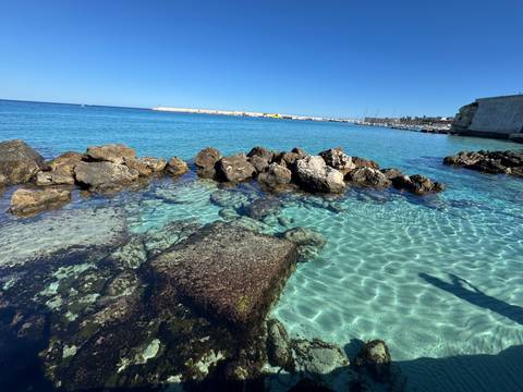 Rocky shoreline with crystal clear water and a distant harbor.