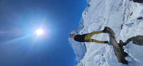 Person standing on a snow-covered rock with a bright sun in the clear sky.