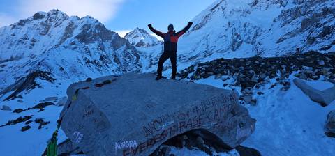 Person triumphantly standing on a boulder with 'Everest Base Camp' written on it.