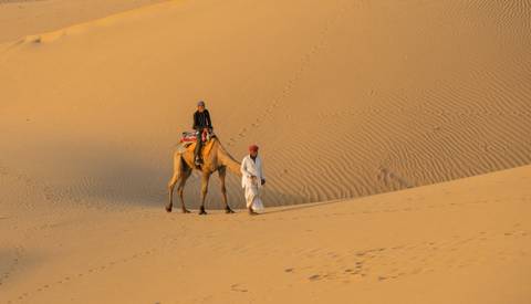 Camel and handler walking through a desert dune.