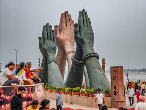 People sitting beside large joined hand statues by a river.