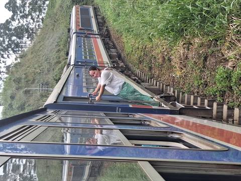       Person hanging out of a train door, scenic greenery and hills visible.
  