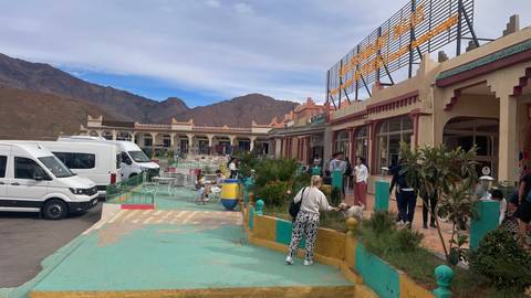       People walking around a colorful marketplace with mountains in the background.
  