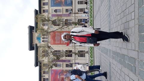 Person posing in a public square with an ornate building in the background.
