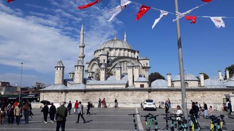 People walking near a mosque with many domes.