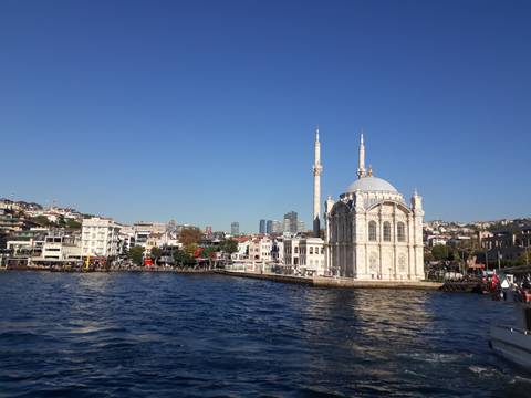       White mosque by the water with a cityscape in the background.
  