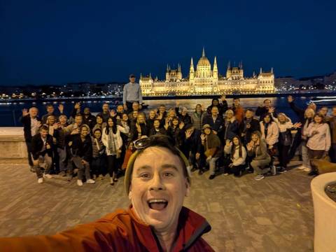       A large group of people posing in front of a lit-up building on the riverside at night.
  