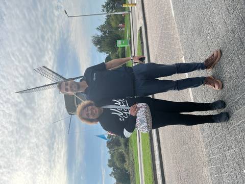 Two people posing in front of a windmill on a sunny day.