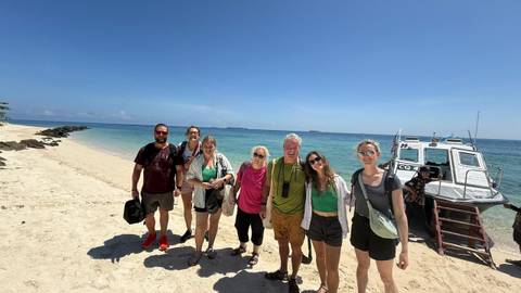       A group of people smiling on a beach with a boat in the background.
  