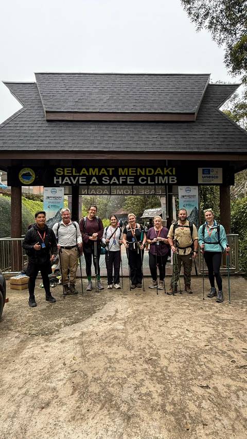       Group of hikers at the entrance of a trail with a sign saying 'Have a Safe Climb'.
  