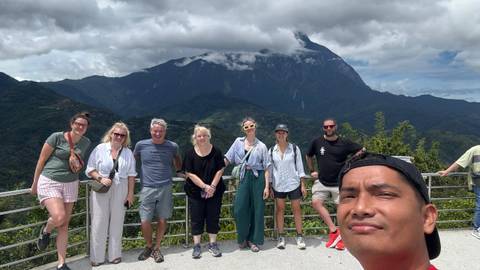       A group of people posing in front of a mountain view on a cloudy day.
  