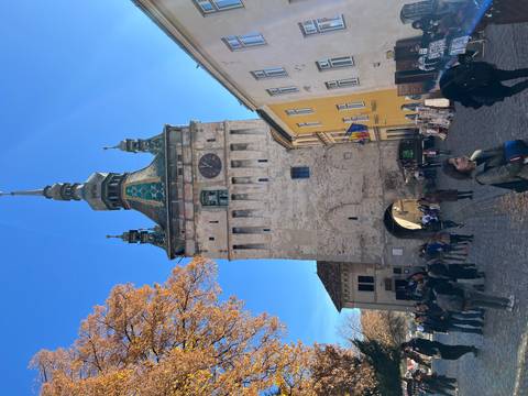       Medieval clock tower with a collection of people in the street.
  