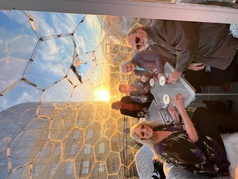 Group of people enjoying drinks inside a dome with a sunset view.