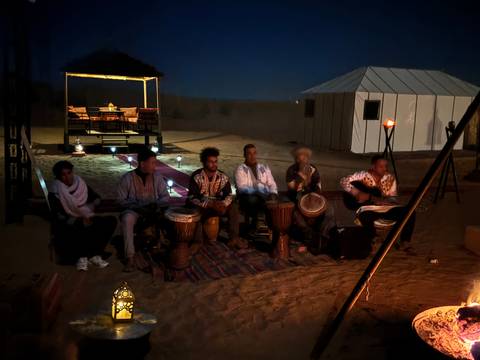       Musicians playing drums and guitars in a desert setting at night.
  