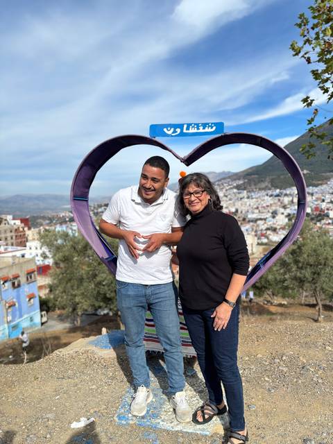 Two people posing in a heart-shaped frame overlooking a city.