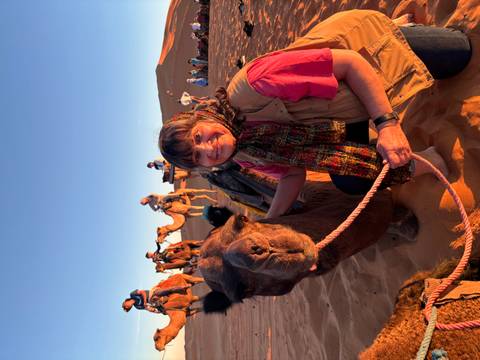 Woman posing next to a camel in a desert landscape.