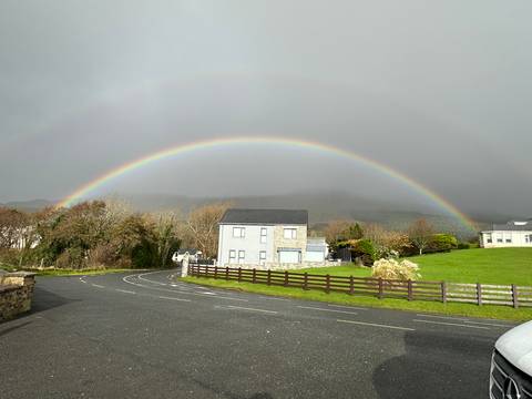 House with a vivid rainbow arching over a cloudy sky
