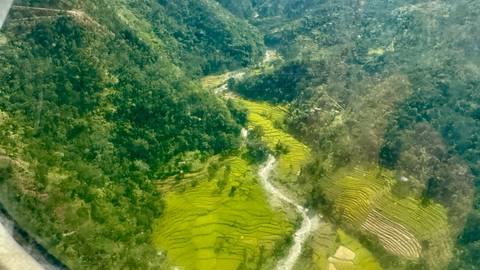 Aerial view of terraced fields and a river in a hilly region.