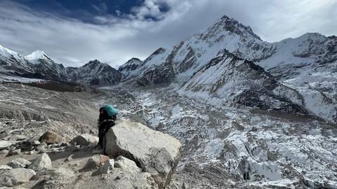 Person resting on a rock in front of snowy mountains.