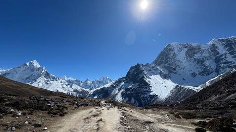 Mountain path with a scenic view of snowy peaks under a bright blue sky.
