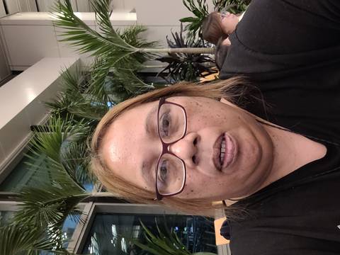       Close-up of a person indoors with palm plants in the background.
  