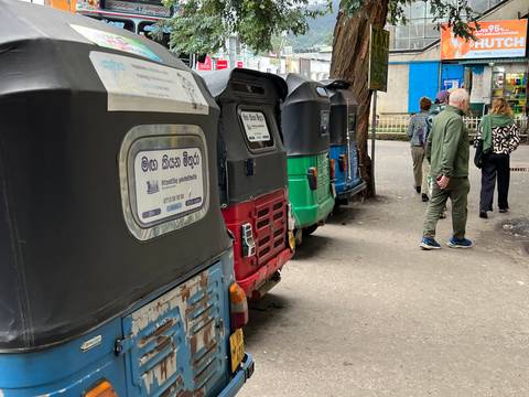 Tuk-tuks lined up on a street with people walking.