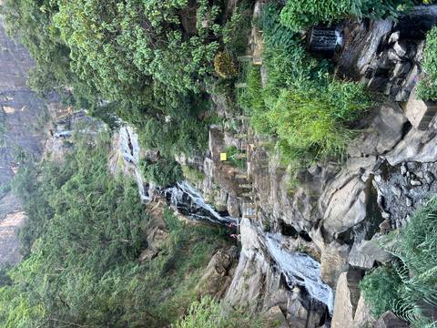 A waterfall cascading down a rocky hill with greenery on the sides.