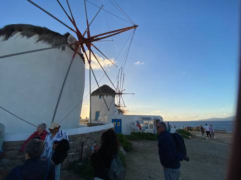       Windmills on an island with people gathering around at sunset.
  