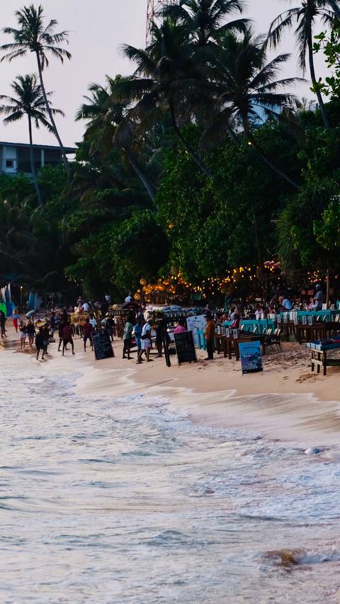       Crowded beach bar scene during the evening with string lights.
  
