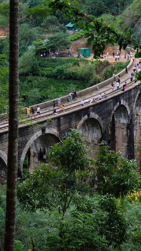       People walking on an old railway bridge.
  