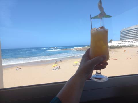 View of beach with a hand holding a drink in the foreground.