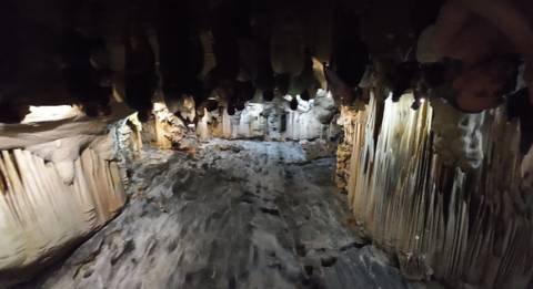       People inside a large cave with stalactites.
  