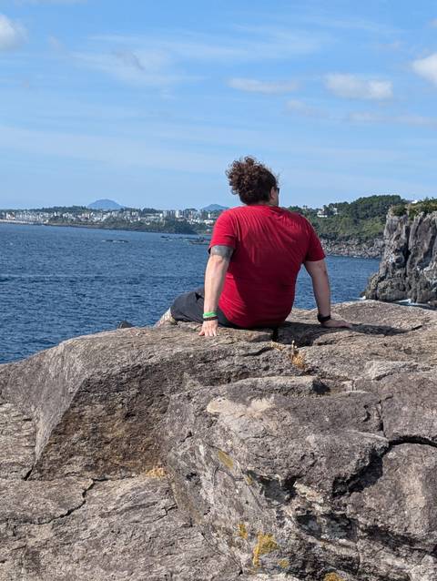 Person sitting on the edge of a cliff overlooking the sea.