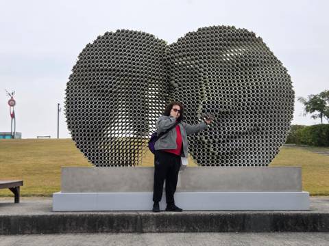 Person posing with a large sculptural installation.