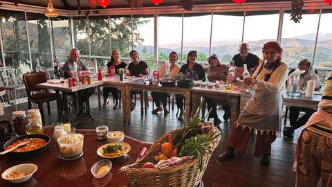 Group of people sitting around a table in a room with large windows overlooking hills.