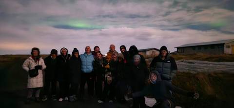       Group of people standing outdoors at night possibly under northern lights.
  