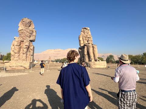 Tourists visiting the Colossi of Memnon with mountains in the background.