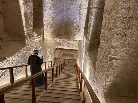 A person walking down wooden stairs into an ancient structure.