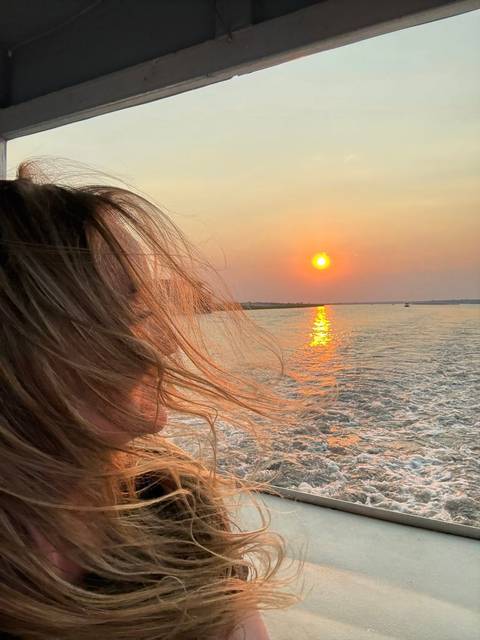       A person on a boat enjoying the sunset on a river.
  