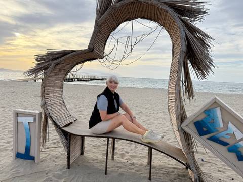 Woman sitting on a heart-shaped bench at the beach.